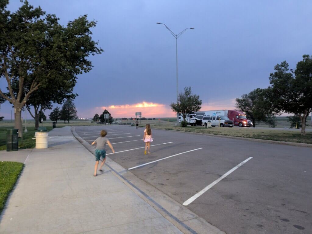 Kids walking across a rest stop parking lot with a stormy, yet colorful sunset sky