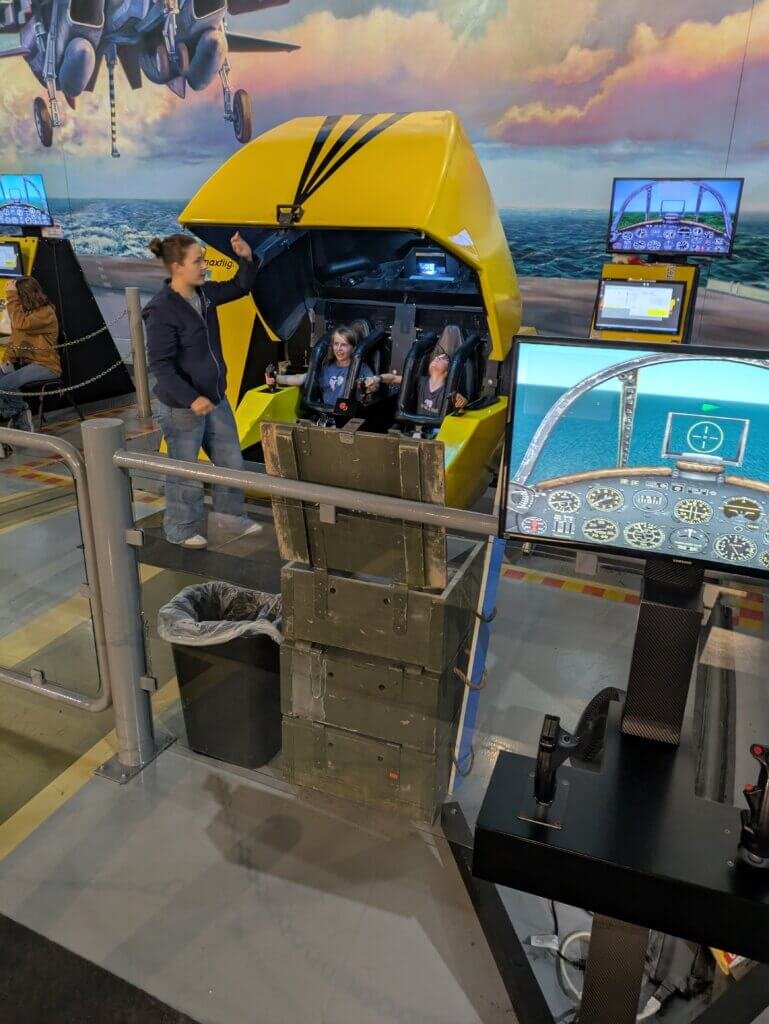 2 kids in flight simulator with instructor standing outside