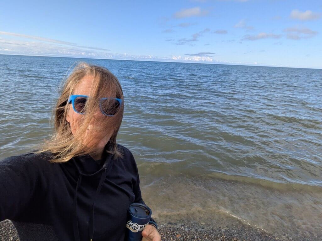 Woman with hair blowing in front of her face with Lake Ontario and blue sky